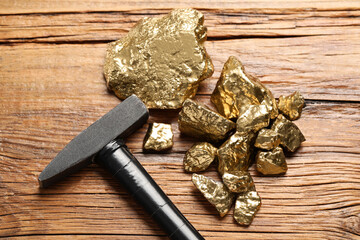 Pile of gold nuggets and hammer on wooden table, flat lay