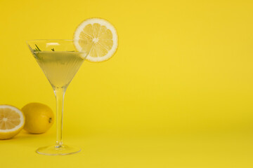 Martini glass of refreshing cocktail with lemon slice, rosemary and fruits on yellow background, space for text