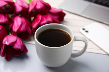 Cup of coffee and beautiful tulips near smartphone on light gray table, closeup