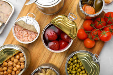 Open tin cans with different preserved products on wooden board, flat lay