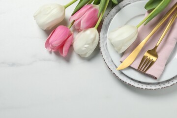 Stylish table setting with cutlery and tulips on white marble background, flat lay. Space for text