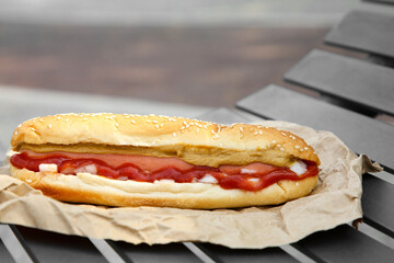 Fresh delicious hot dog with sauce on black bench outdoors