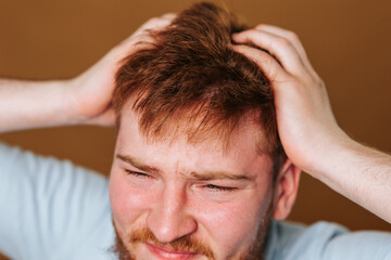 A studio shot of a guy with a head full of itchy hair, scratching his scalp in discomfort.