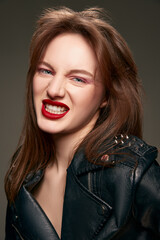 Attractive, young, beautiful girl with red lips makeup posing in trendy leather jacket against grey studio background. Emotions. Concept of skin care, cosmetology, cosmetics, natural beauty, fashion