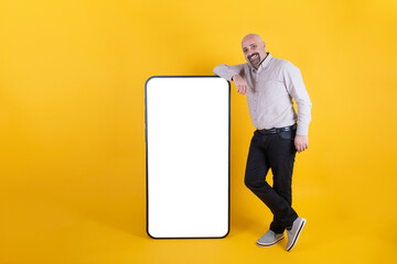 Mobile app advertisement, man leaning big smartphone for mobile app advertisement. Full body length of happy smiling middle aged male near big huge white empty screen cellphone mock up. Copy space.