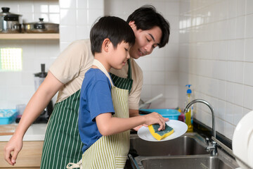 Happy smiling Young Asian father and son washing dishes in kitchen at home