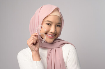 Young smiling muslim woman with hijab holding invisalign braces in studio, dental healthcare and Orthodontic concept.