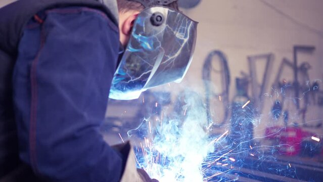 Person with special safety equipment welding a metal joint in slow motion in workshop