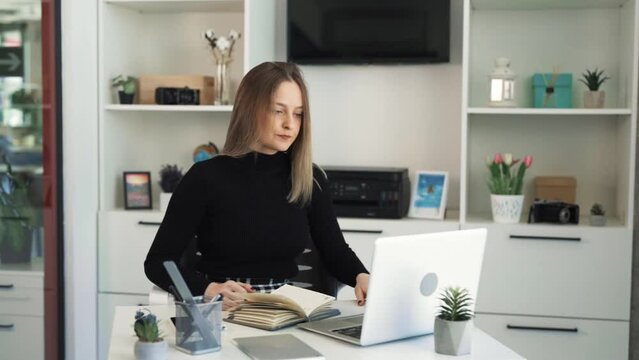 The blonde woman is sitting at a table and talking via Zoom, she is emotional and cheerful, she is angry, aggressive, irritated, dissatisfied with the conversation with the interlocutor