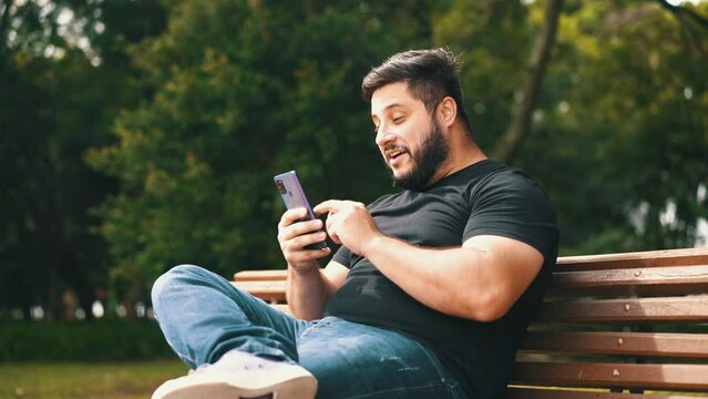 Young man celebrating good news recieved on his cell phone while seated at a park bench	