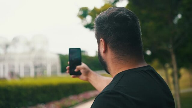 Young man taking a picture of the greenhouse and garden with cell phone of Botanical Garden, Located in Curitiba, Brazil	
