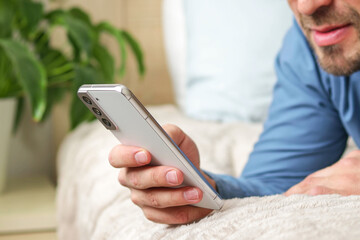 Man using mobile phone, playing game, shopping online, ordering delivery, relaxing on sofa