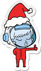 sticker cartoon of a pretty astronaut girl giving thumbs up wearing santa hat