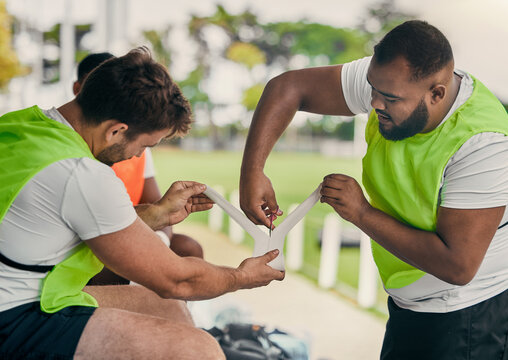 Men, cutting bandage or rugby team on fitness break, exercise workout or training in a sports game. Preparation, friends or group of people in practice match with tape, strap or wrap on stadium bench