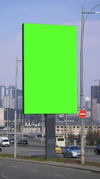 Big green screen billboard with city traffic background. Blurred transport moving on road. Vertical lightbox for advertising, cars driving in town