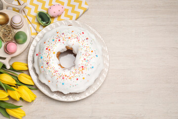 Easter cake with sprinkles, painted eggs and tulips on white wooden table, flat lay. Space for text