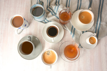 Several different cups and mugs with coffee and tea drinks on a light table with a blue gray towel, high angle view from above, selected focus