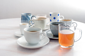 Tea and coffee cups in different styles on a white wooden table against a light gray wall, copy space, selected focus
