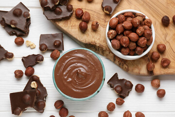 Bowl with tasty paste, chocolate pieces and nuts on white wooden table, flat lay