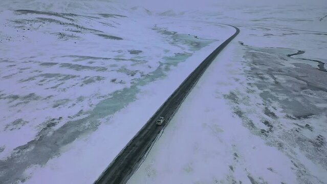 suivi par drone en hauteur d'une voiture van sur une route enneig&eacute; au milieu d'une nature sauvage d'Islande recouverte par la neige avec une route noire et des fleuves gel&eacute;s 