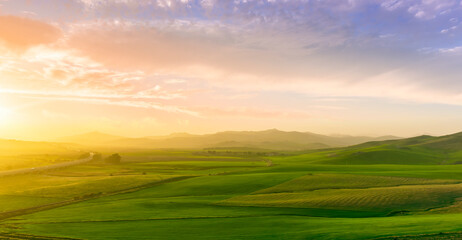 countryside sunset in green hills of spring fields with old castle farm and mountains on background of evening landscape