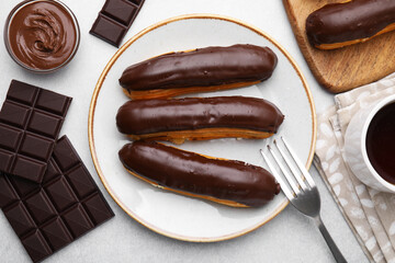 Delicious eclairs and chocolate on grey table, flat lay