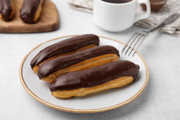 Delicious eclairs covered with chocolate on grey table