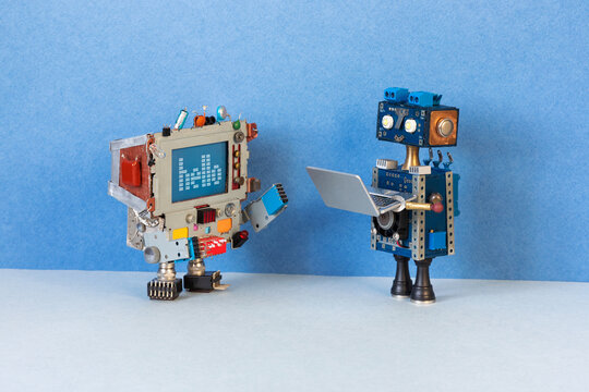 Modern and retro vintage technology concept. Toy personal computer character greets a robot holding a modern laptop.