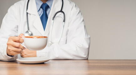 Doctor in uniform with a stethoscope holding a coffee cup while sitting at the desk