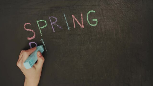 Timelapse close-up a child hand writes a spring break on a blackboard with colored chalk and draws the sun. The concept of vacation, childhood, school