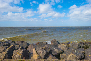 Dike along a stormy lake below a blue sky and white clouds in winter, Markerwaard, Almere, Flevoland, The Netherlands, March 13, 2023