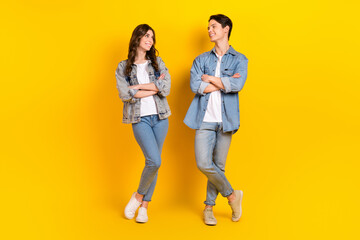 Full length portrait of two cheerful satisfied people crossed arms look each other isolated on yellow color background