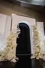 Wedding reception for luxury ceremony in hall restaurant. Copy space. Black photo wall, arch place decorated petal, flower. Celebration baptism concept. Trendy decor for birthday party in banquet area