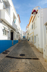 Fototapeta na wymiar Narrow street of Salema. Whitewashed houses of the small authentic fishing village. Faro, Algarve, Southern Portugal.