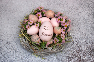 Cesta decorativa de Pascua con flores y un huevo de Pascua inscrito con el texto Felices Pascuas.