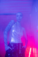 sexy woman in metallic top standing with hands in pockets of the black leather skirt in blue and pink foggy lighting.