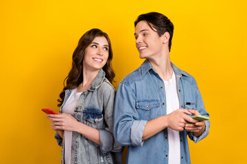 Portrait of friendly positive partners toothy smile look each other hold smart phone isolated on yellow color background