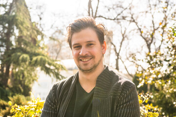 A man sits in a park in the sunlight wearing a black jacket with a black shirt