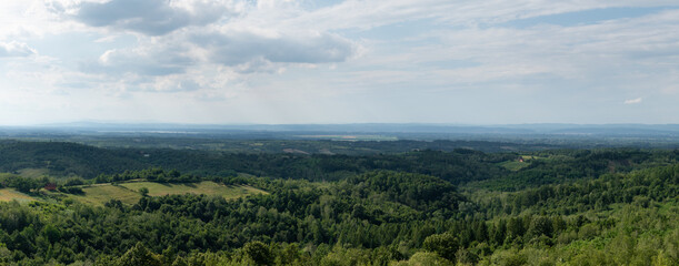 Hilly countryside panorama, distant valley filled with haze, scattered village and lush forests