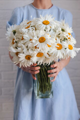 Woman in blue dress holding bouquet of chamomile flowers