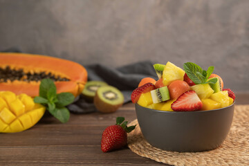 Fruit salad in the gray bowl. Pineapple, papaya, kiwi, grapes, strawberry.