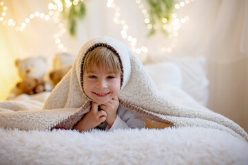 Little cute preschool boy, holding cute teddy bear, hiding under blanketl, playing at home in bedroom