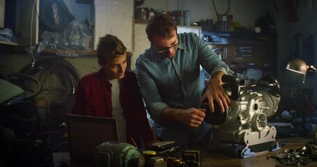 Portrait of a Happy Teenage Boy and his Father in Workshop Working Together on Fixing an Engine. Man Explaining and Teaching his Son About Mechanics. They are Bonding, Sharing their Hobby