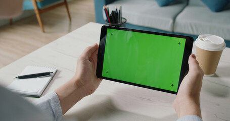 Freelance worker at home holding a tablet computer with green template screen, watching a webinar, studying online 