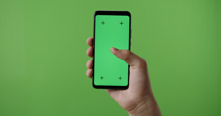 man's hand holding a mobile telephone with a vertical green screen in tram chroma key smartphone...