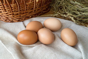 Pile of hen eggs near wicker basket and straw hay nest. Organic farm food.