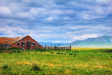 Beautiful scenery with old abandoned farm. Ruined building with a wooden fence and green field at...