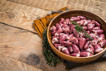 Raw chicken hearts in a wooden plate with herbs. Organic offals. Wooden background. Top view. Copy space