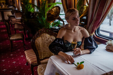 Girl in retro train in beautiful dress sits at a table with yellow rose by the window