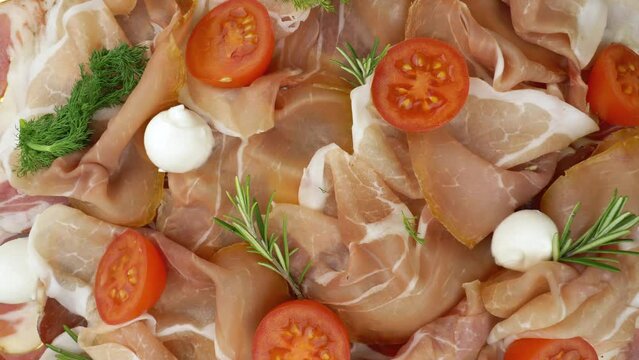 Raw ham. Slices of Jinhua or prosciutto crudo with fresh rosemary, mozzarella, and tomatoes. View from above